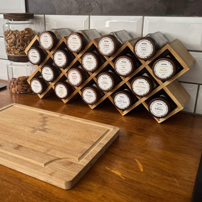 Présentoir à épices en bois Épices Moralès garni de 18 fioles, posé en cuisine près d’une planche à découper.