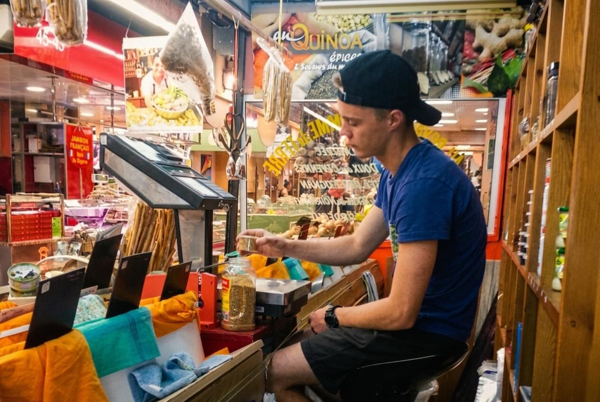 Sébastien à l'étal familial des Halles de Nîmes, pesant des épices au détail — les débuts qui ont inspiré la création d'Épices Moralès.